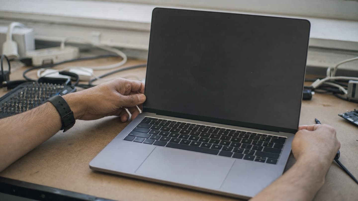 A laptop opened on a bench beside a screwdriver set and cables during a display diagnosis.