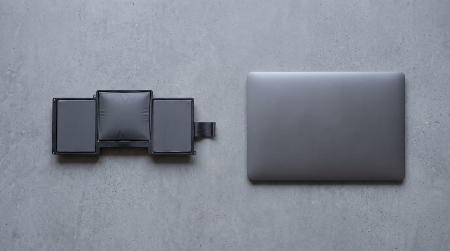 A laptop battery removed from its machine, its middle cell visibly domed and lifting off the surface, laid beside the bowed aluminium bottom panel it came out of.