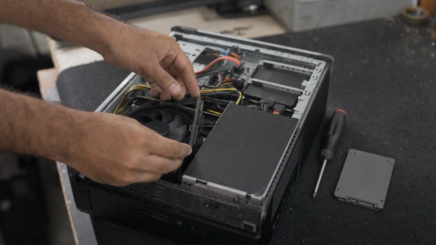 An open desktop PC on a bench beside a screwdriver and a spare SSD, mid-upgrade.