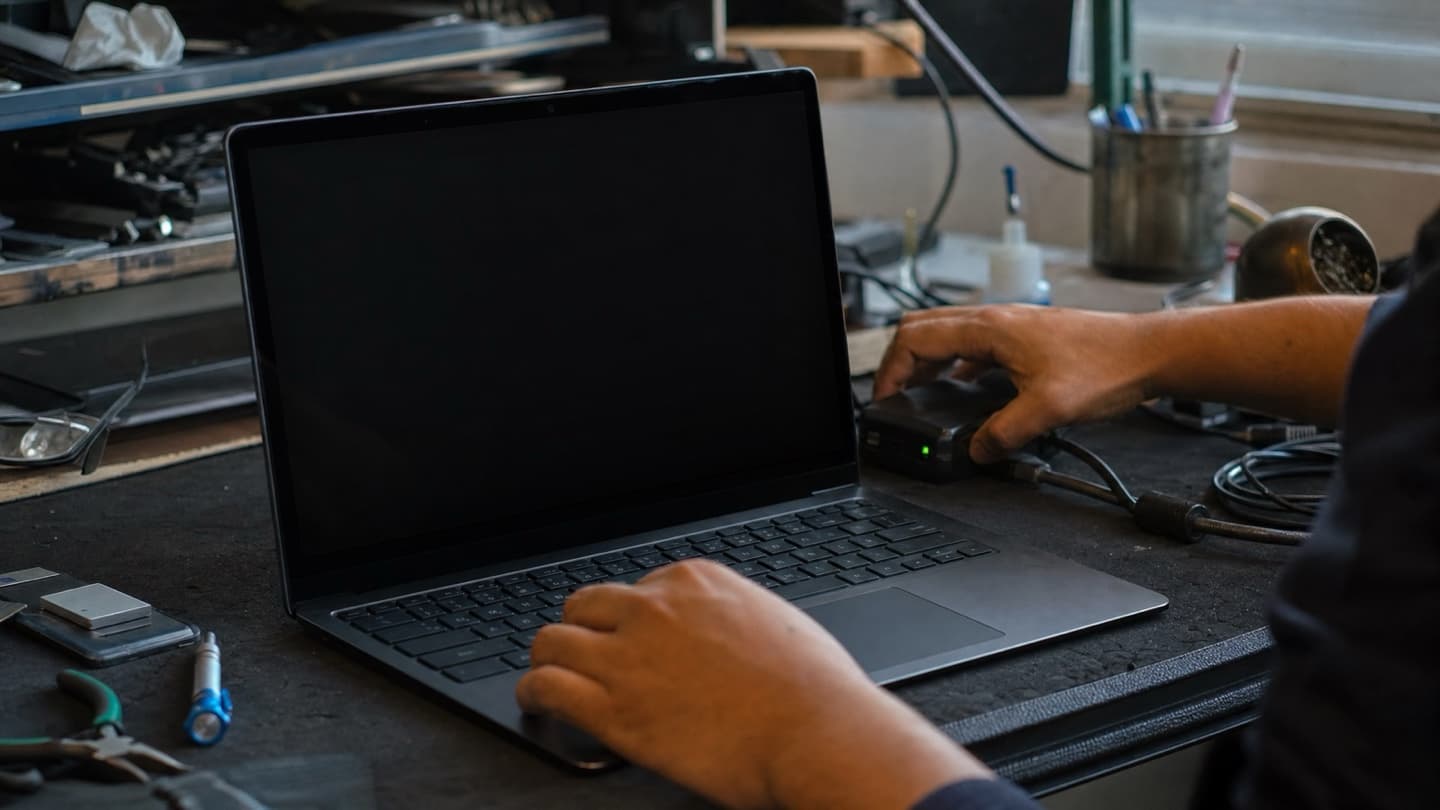 Hands at a bench running a malware scan on a laptop connected to a diagnostic tool.