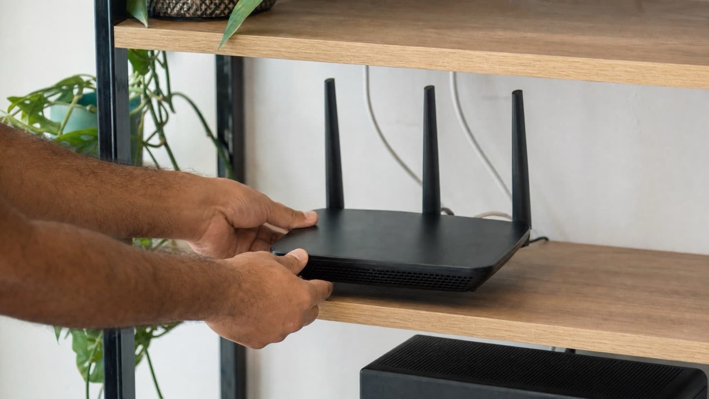 A router being repositioned on an open shelf away from a cabinet during a home visit.